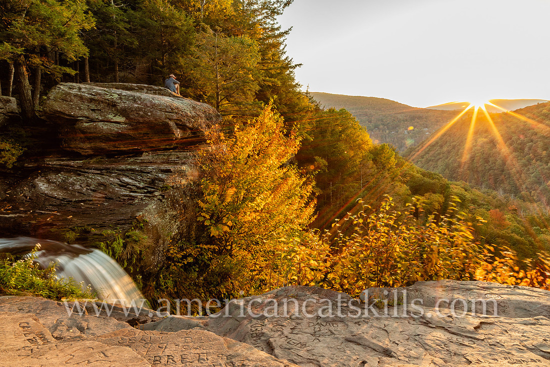 Photograph of a man sitting on a ledge watching the sunset over Kaaterskill Clove in the northern Catskills.