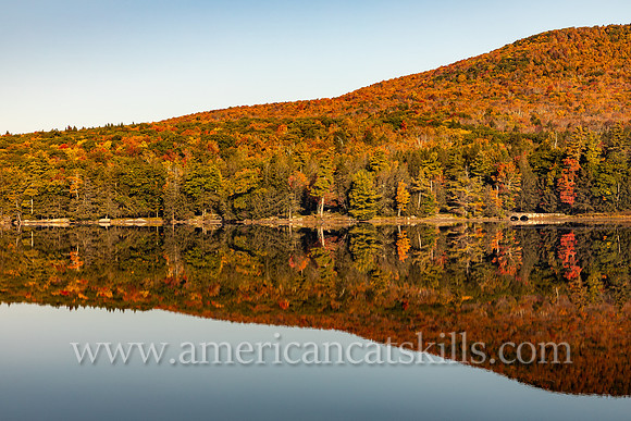 Photograph of a mountain in autumn reflecting in the lake at North-South Lake in the Catskills.