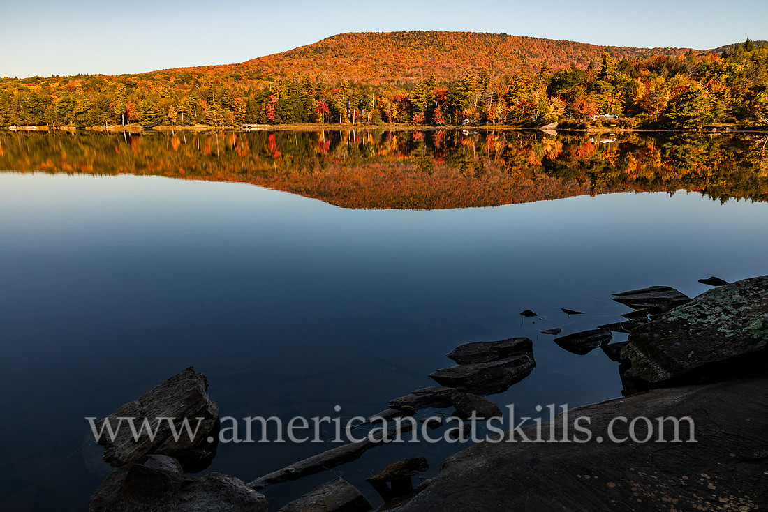 Photograph of a mountain reflecting in the lake with rocks in the foreground at North-South Lake in the Catskills.