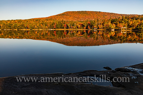 Photograph of a mountain reflecting in the lake with rocks in the foreground at North-South Lake in the Catskills.