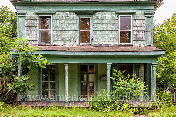 Green abandoned home in Deposit, Delaware County with “For Sale” sign in the window.