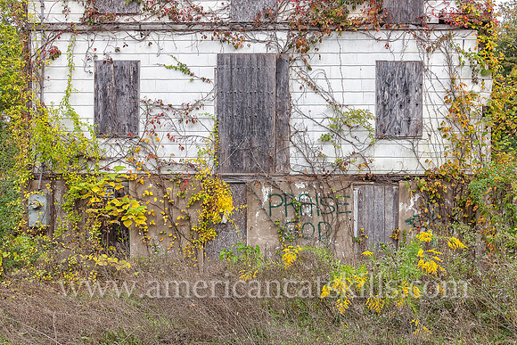 Abandoned building with the words “Praise God” spray-painted on the front of the building; building overgrown with vines; located at Kingston in Ulster County, New York.