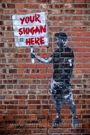 Kingston, New York mural on a brick wall with a silhouette of a young man holding a sign saying “Your Slogan Here.”