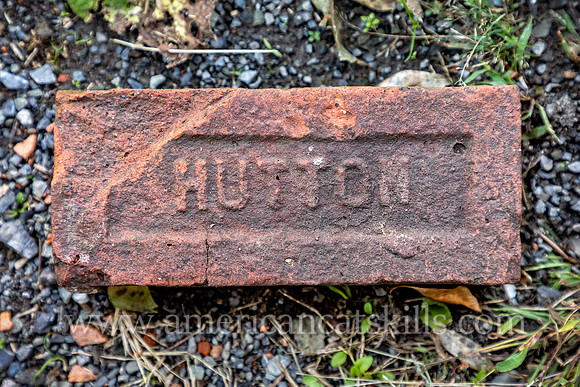 Close up of a brick in the sidewalk with the word “Hutton” imprinted on the face of the brick, as manufactured by the Hutton Brick Company of Kingston, New York.