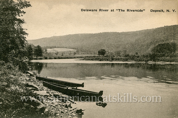 Two canoes are set upon the riverside along the Delaware River at the town of Deposit, New York in this vintage Catskills postcard.