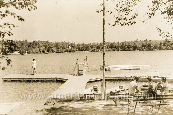 A group of four boys hang out at the docks in the peaceful lake scene taken by well-known photographer Otto Hillig of Liberty, New York.